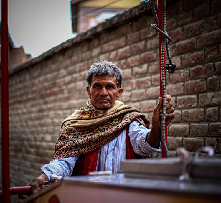 An Elderly Man Wearing A Scarf While Holding On His Cart