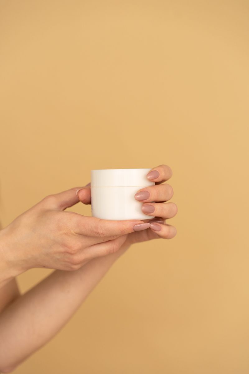 Hands presenting a cosmetic cream jar on a warm beige background