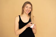 穿着黑色背心的快乐女人在室内拿着护肤霜罐，背景中性