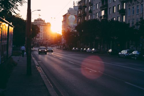 Free Urban street scene with cars and buildings during sunrise, capturing modern city life. Stock Photo