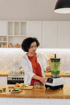 Young woman blending vegetables and fruits in a contemporary kitchen setting for a healthy lifestyle.