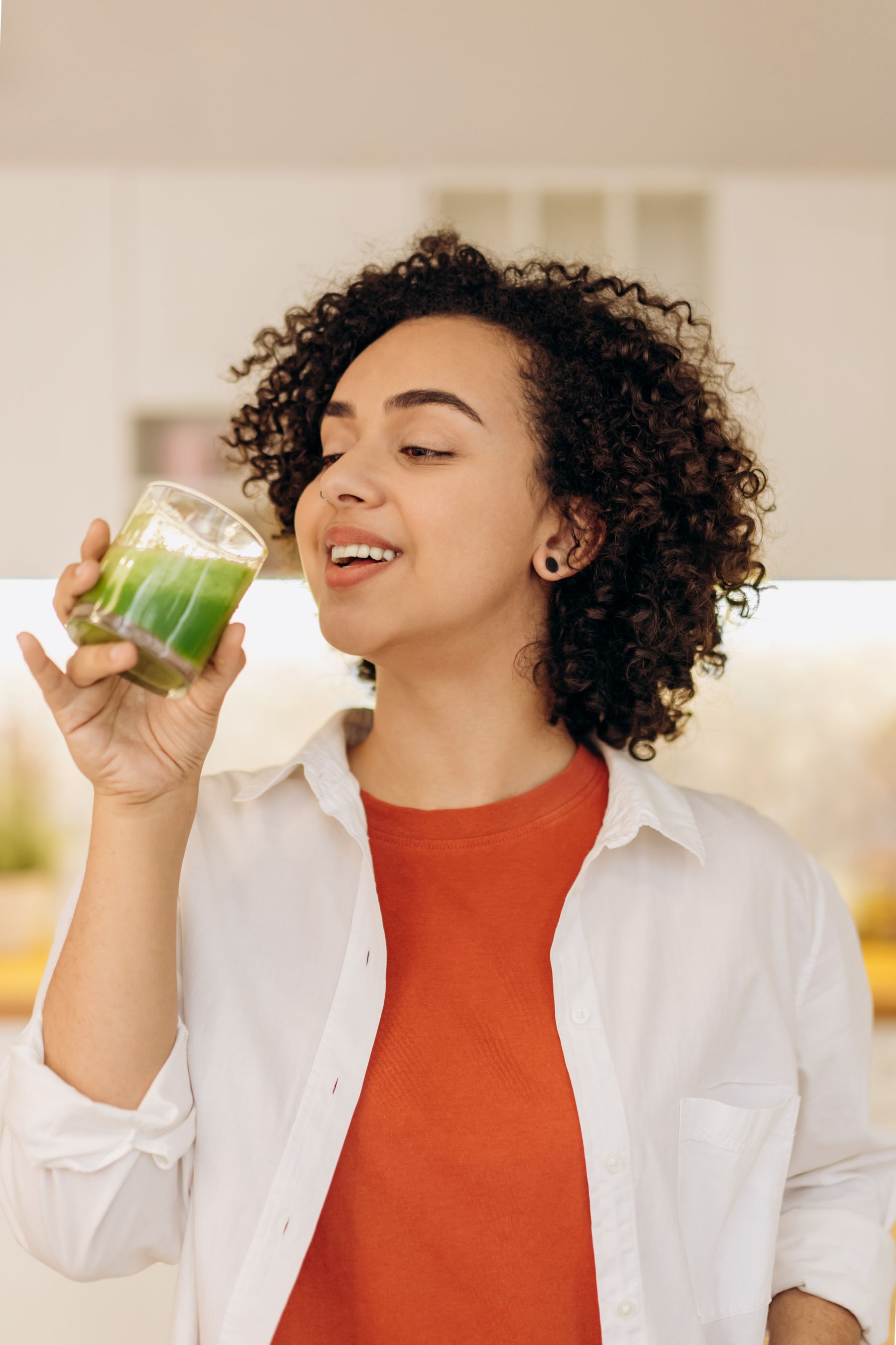 A smiling woman enjoying a fresh green smoothie in a bright home kitchen