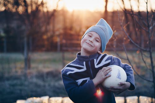 Free Selective Focus Photography of Boy Wearing Blue United Kingdom Print Zip-up Jacket Carrying White Ball Stock Photo