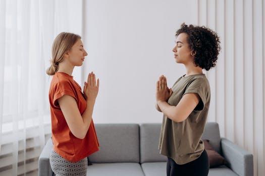 Two women practicing yoga and mindfulness indoors, focusing on relaxation and wellbeing.