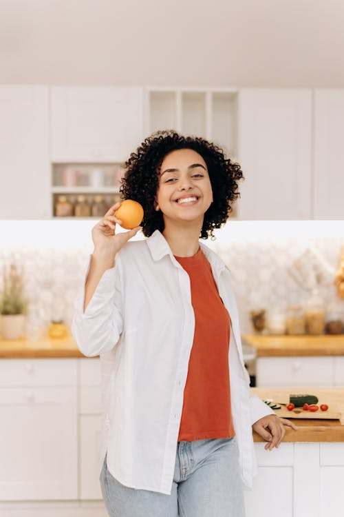 Woman in White Long Sleeve Shirt Holding Orange Fruit