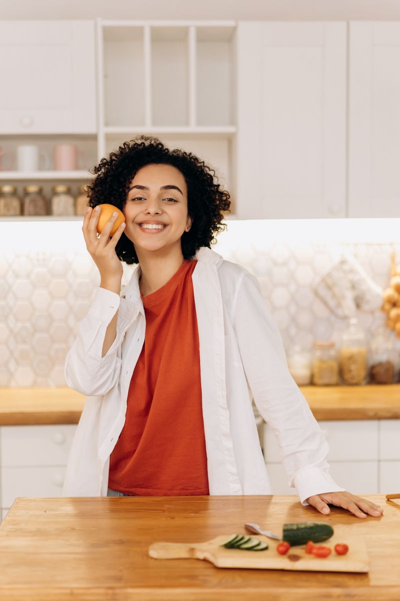 A woman holding an orange in a bright kitchen