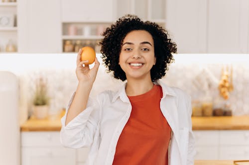 Woman in White Button Up Shirt Holding Orange Fruit