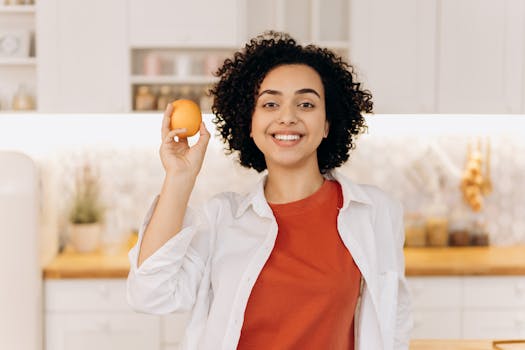 Smiling woman holding an orange, symbolizing a fresh and healthy lifestyle in a modern kitchen.