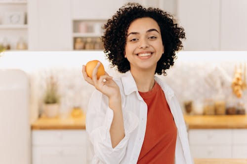 Woman in White Button Up Shirt Holding Orange Fruit