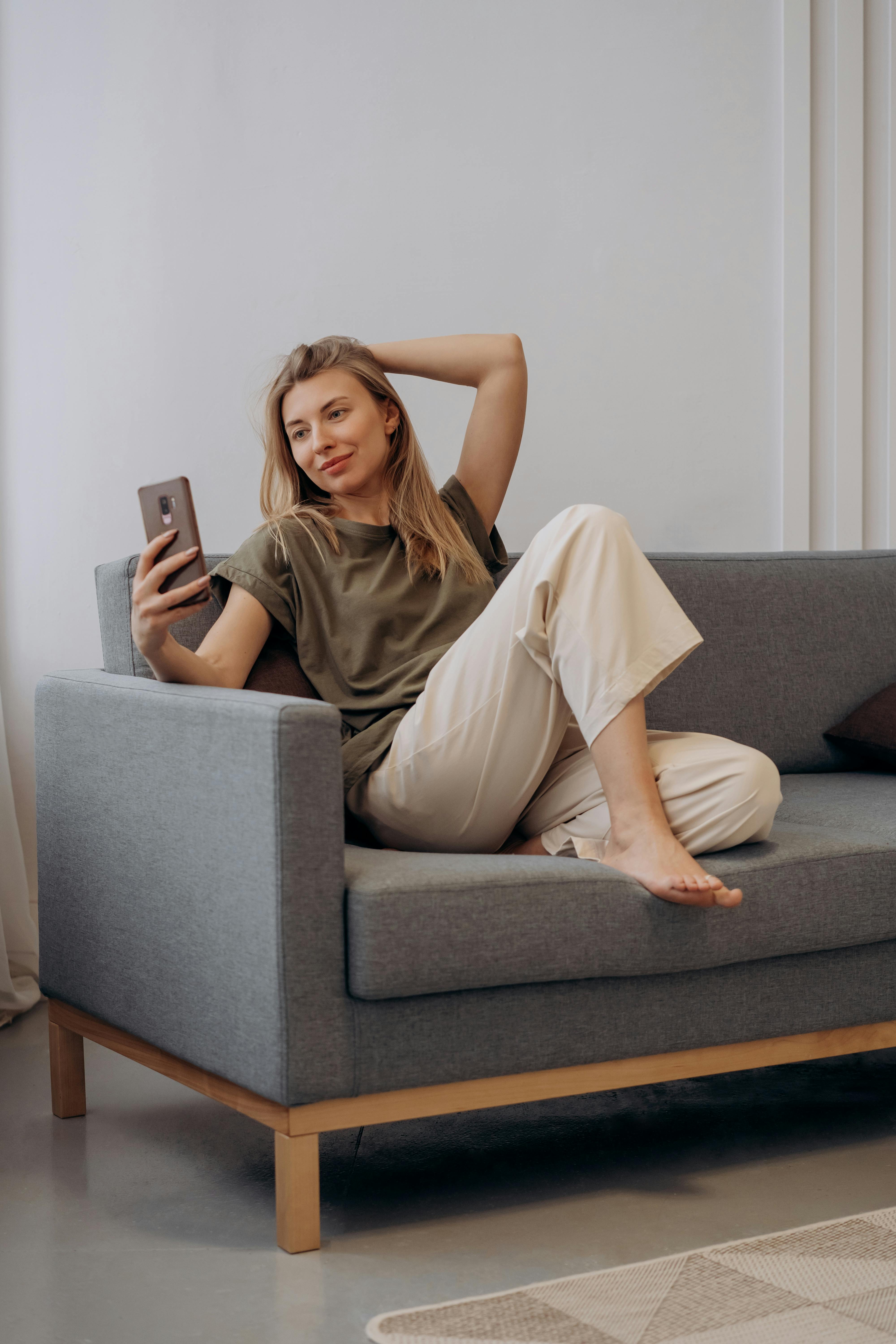 woman sitting on gray couch using her smartphone