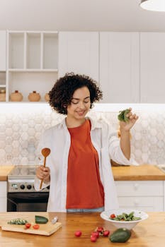 A woman in a kitchen preparing a fresh and healthy vegetable salad with cucumbers and cherry tomatoes.