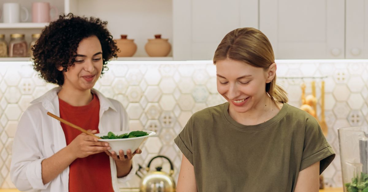 Two women cooking together in a cozy kitchen, preparing healthy meals for advanced menstrual cycle nutrition.