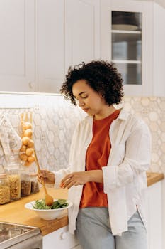 Curly-haired woman in a kitchen making a fresh salad, embracing a healthy lifestyle.
