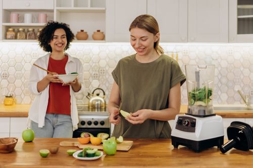 Free Two women enjoying a healthy meal preparation in a modern kitchen setting, smiling and happy. Stock Photo
