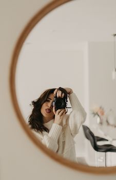 Young woman in white sweater taking a playful selfie in a round mirror indoors.