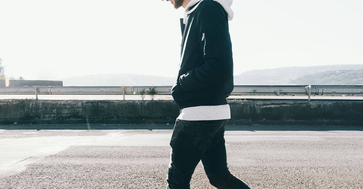 Rüyada Yürüyüşe Çıkmak - Rüya Tabiri ve Anlamı - Casual male in a cap and hoodie walks along a sunny urban street.