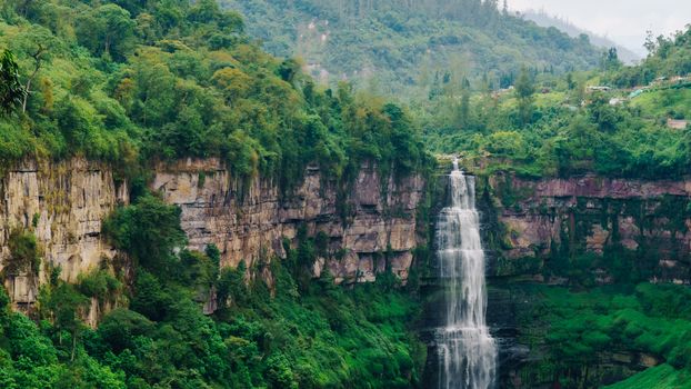 Beautiful waterfall cascading down a verdant mountain cliff surrounded by dense forest.
