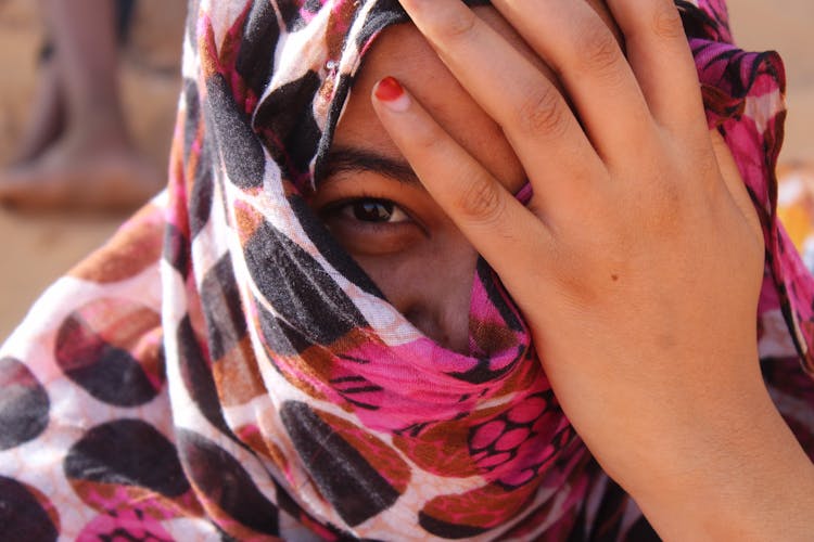 Close-Up Photo Of Woman Covering Her Face With Her Hand While Looking At Camera