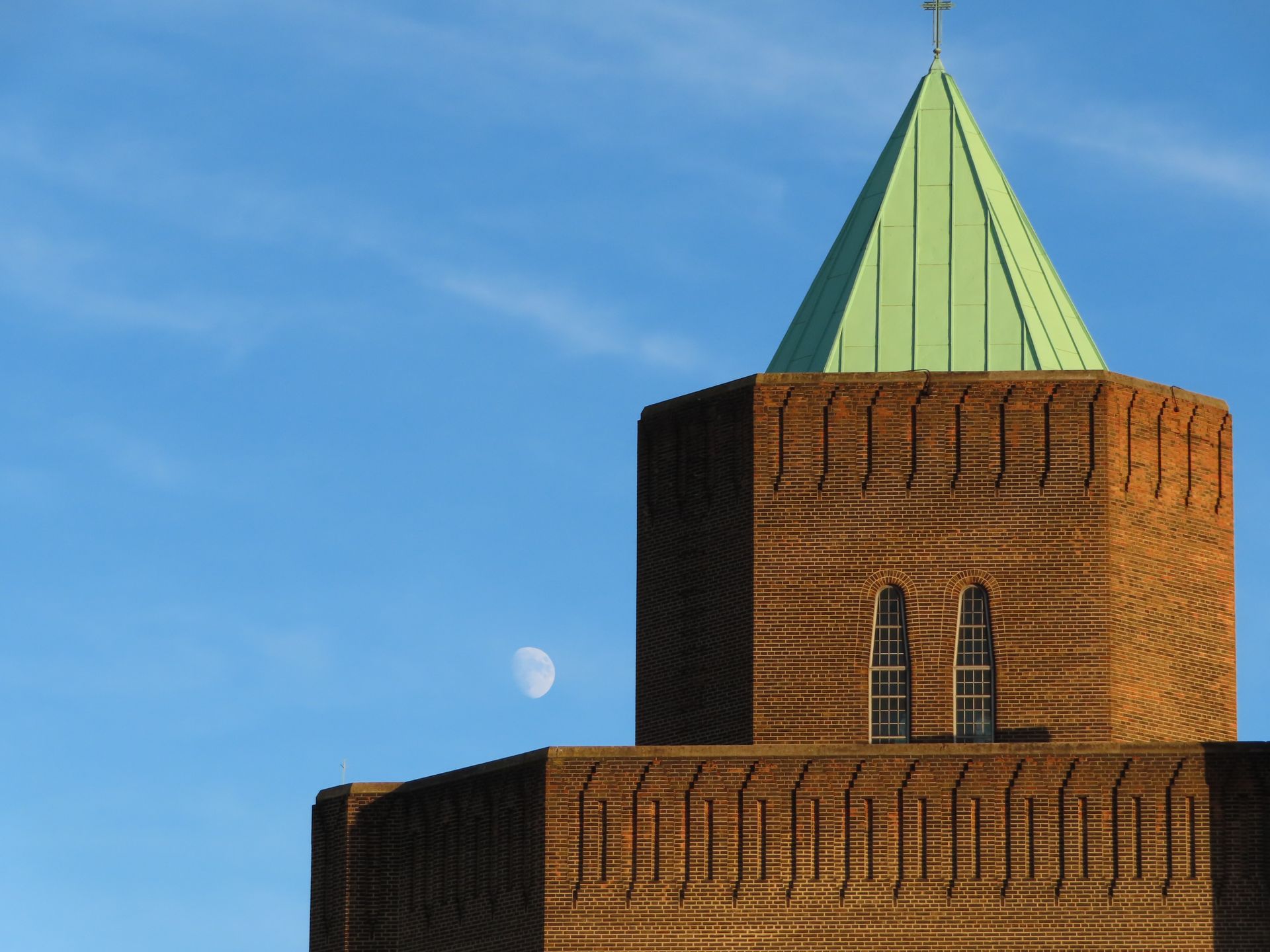 A scenic view of a brick tower with a copper roof and moon against a clear blue sky.