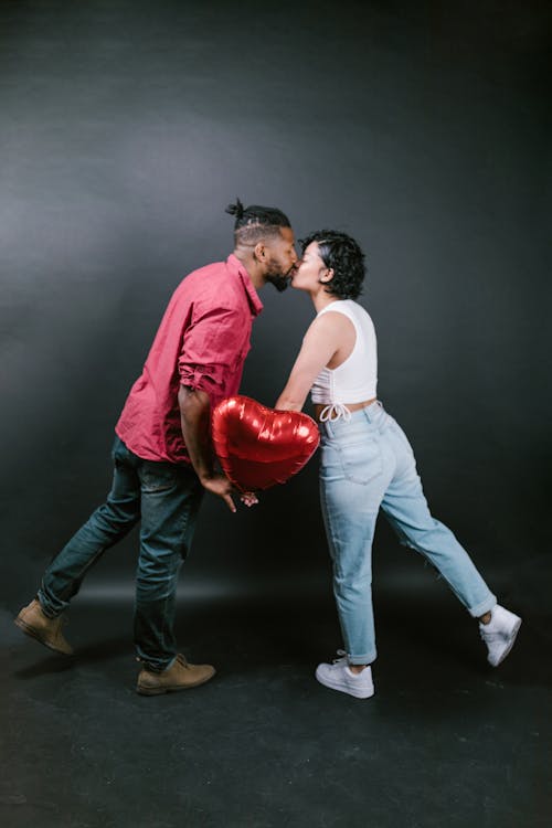 Couple Kissing While Holding a Red Heart Shaped Balloon