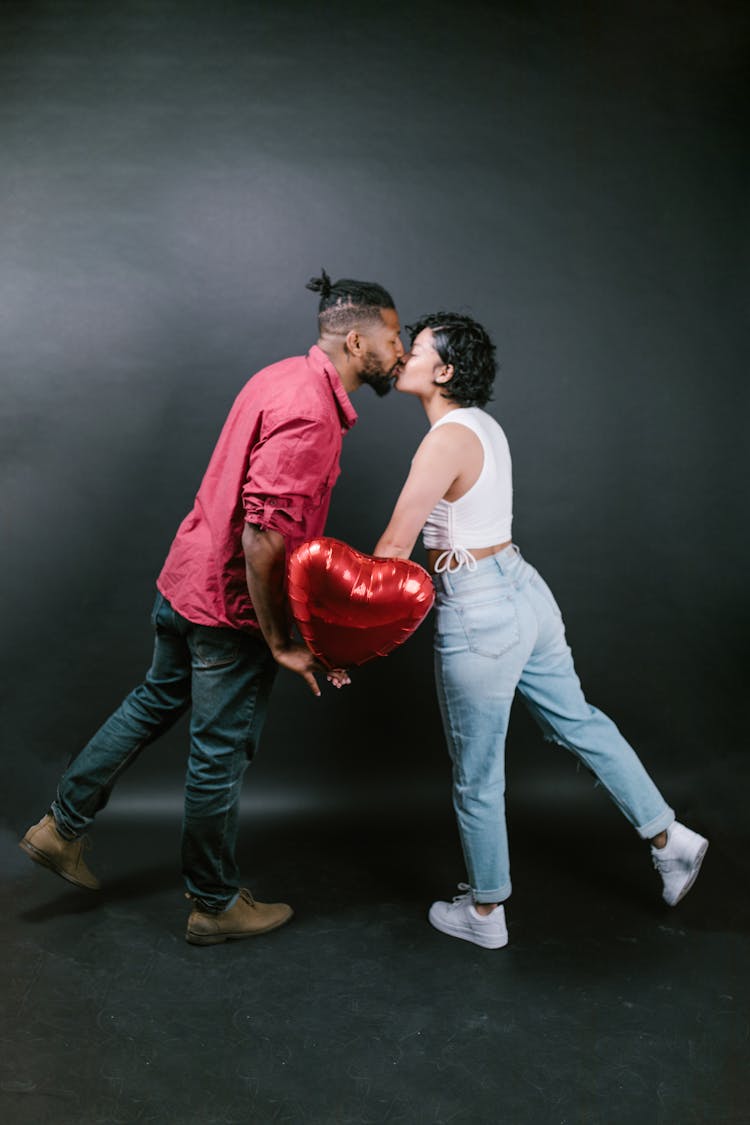 Couple Kissing While Holding A Red Heart Shaped Balloon