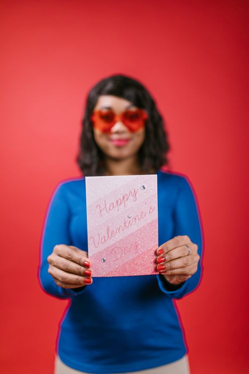Free Woman holding a Valentine's card against a vibrant red background, expressing love and joy. Stock Photo