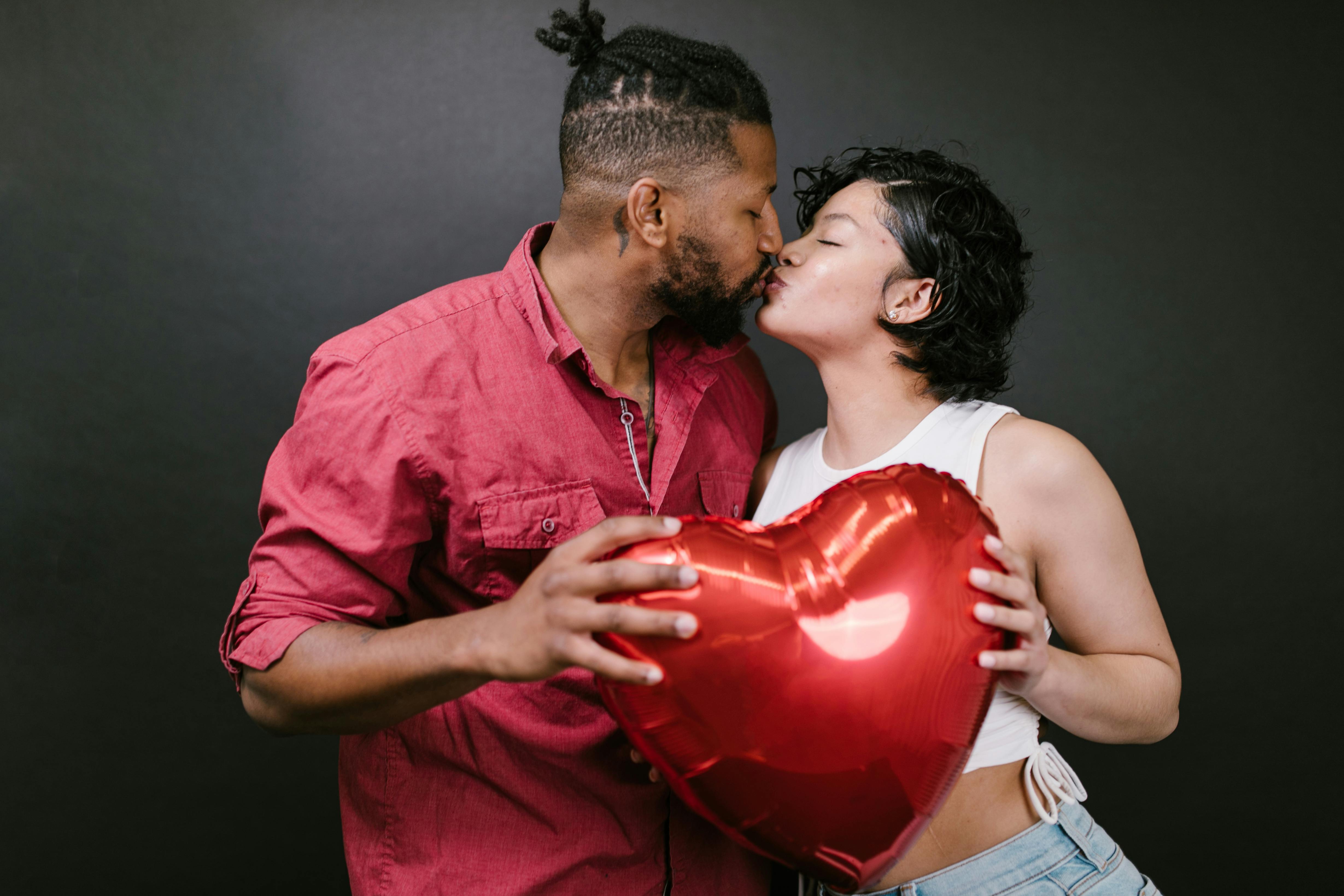 couple kissing while holding a red heart shaped balloon