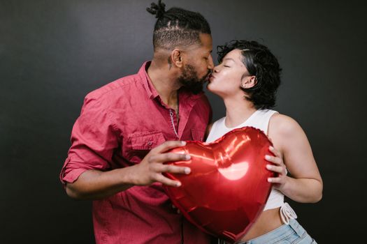 Couple Kissing While Holding a Red Heart Shaped Balloon