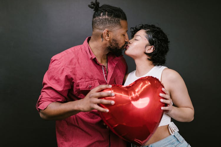 Couple Kissing While Holding A Red Heart Shaped Balloon