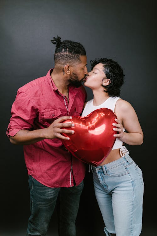 Couple Kissing While Holding a Red Heart Shaped Balloon