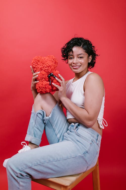 Woman in White Tank Top and Blue Denim Jeans Holding Teddy Bear Shaped Gift