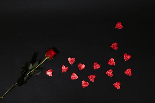 A dramatic image of a single red rose with scattered heart shapes on a dark background, perfect for Valentine's themes.