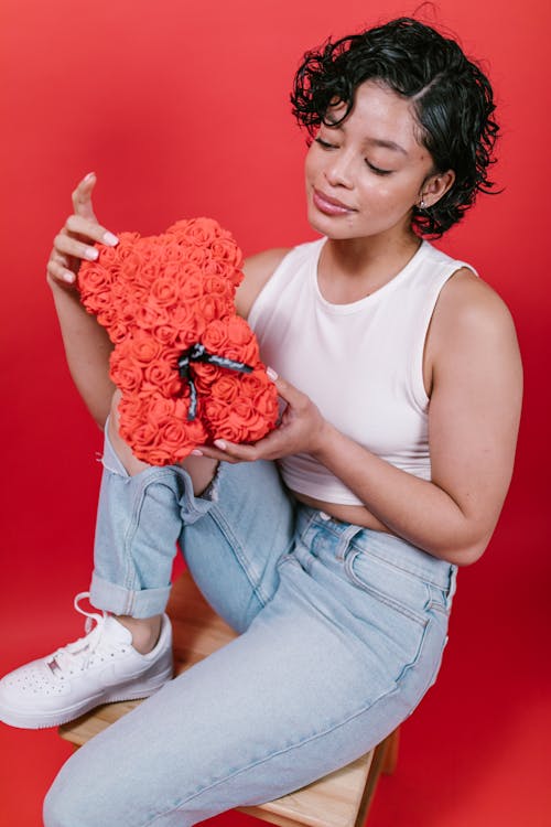 Woman in White Tank Top and Blue Denim Jeans Holding Teddy Bear Shaped Gift