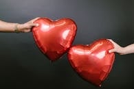 Two Persons Holding Two Red Heart Shaped Balloons