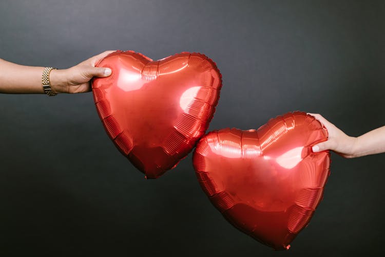 Two Persons Holding Two Red Heart Shaped Balloons