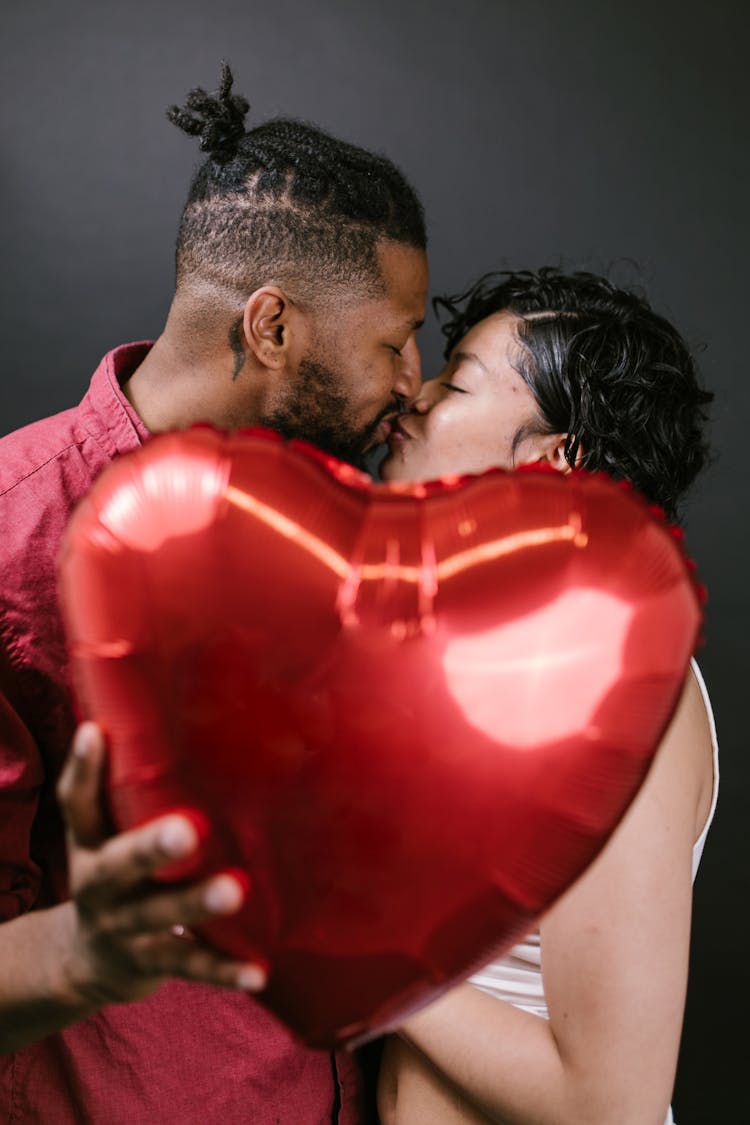 Couple Kissing While Holding A Red Heart Shaped Balloon