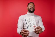 Smiling man holding an 'I love you' card on a vibrant red background, perfect for Valentine's Day themes.