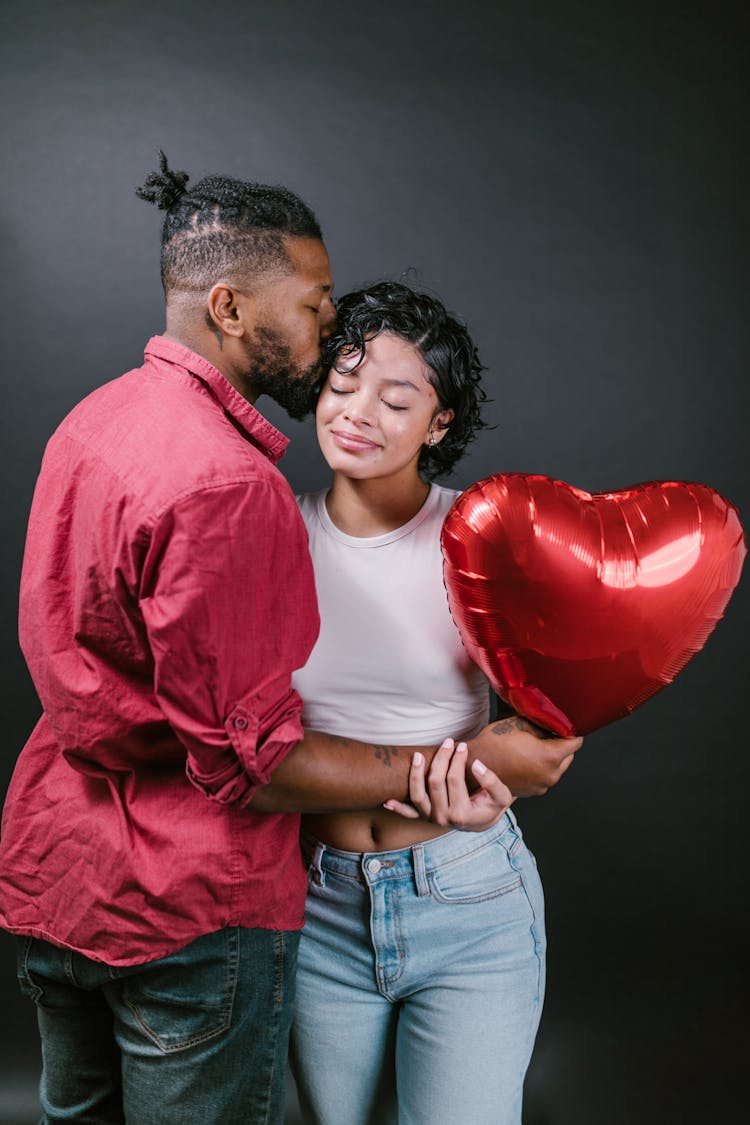 Man Kissing His Woman While Holding A Red Heart Shaped Balloon