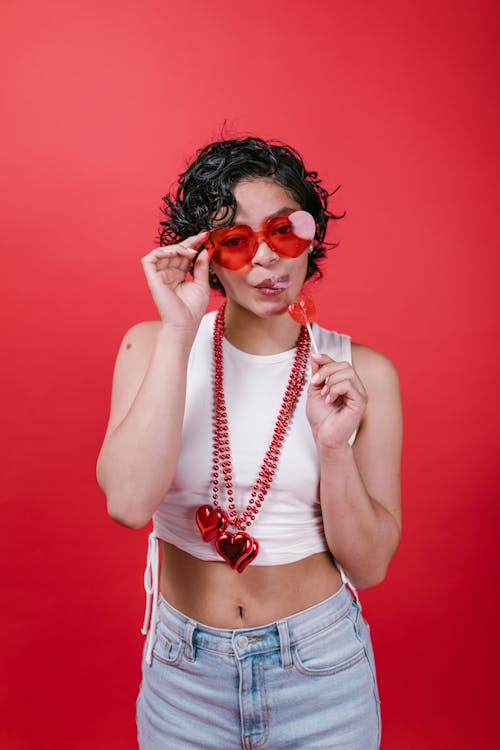 Woman in White Tank Top Holding a Red Heart Shaped Lollipop