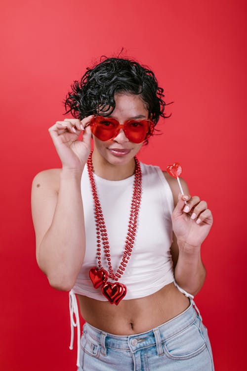 Free Woman in White Tank Top Holding a Red Heart Shaped Lollipop Stock Photo