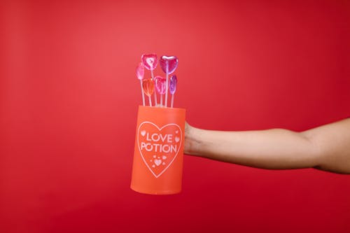 Person Holding Red Mug With Heart Shaped Lollipops