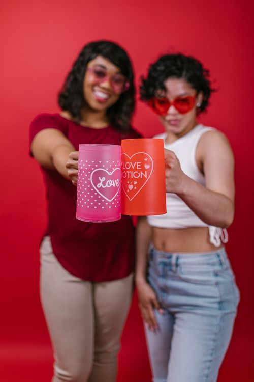 Free Two women in festive moods holding decorative mugs with love themes on a red background. Stock Photo