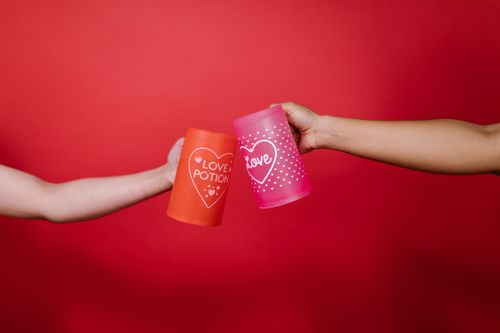 Free Two arms toasting with love-themed mugs against a vibrant red background. Stock Photo