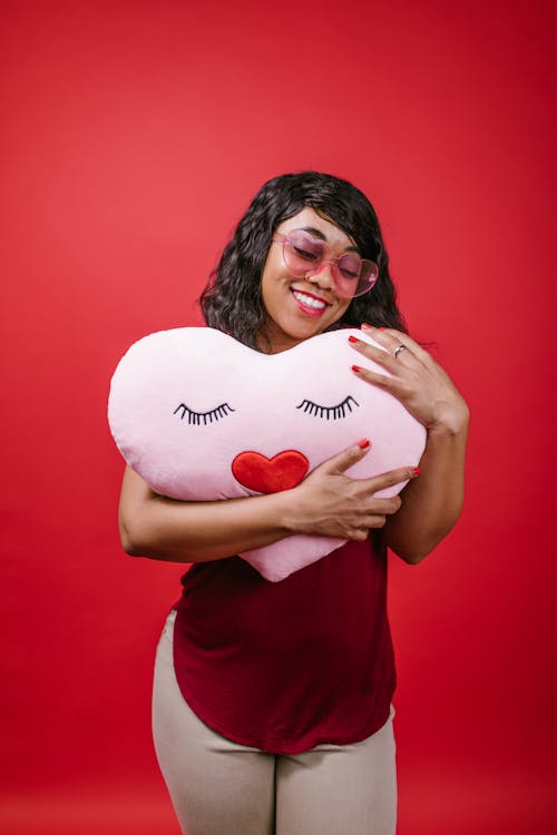 Woman in Red Crew Neck Shirt Holding a Pink Heart Shaped Pillow