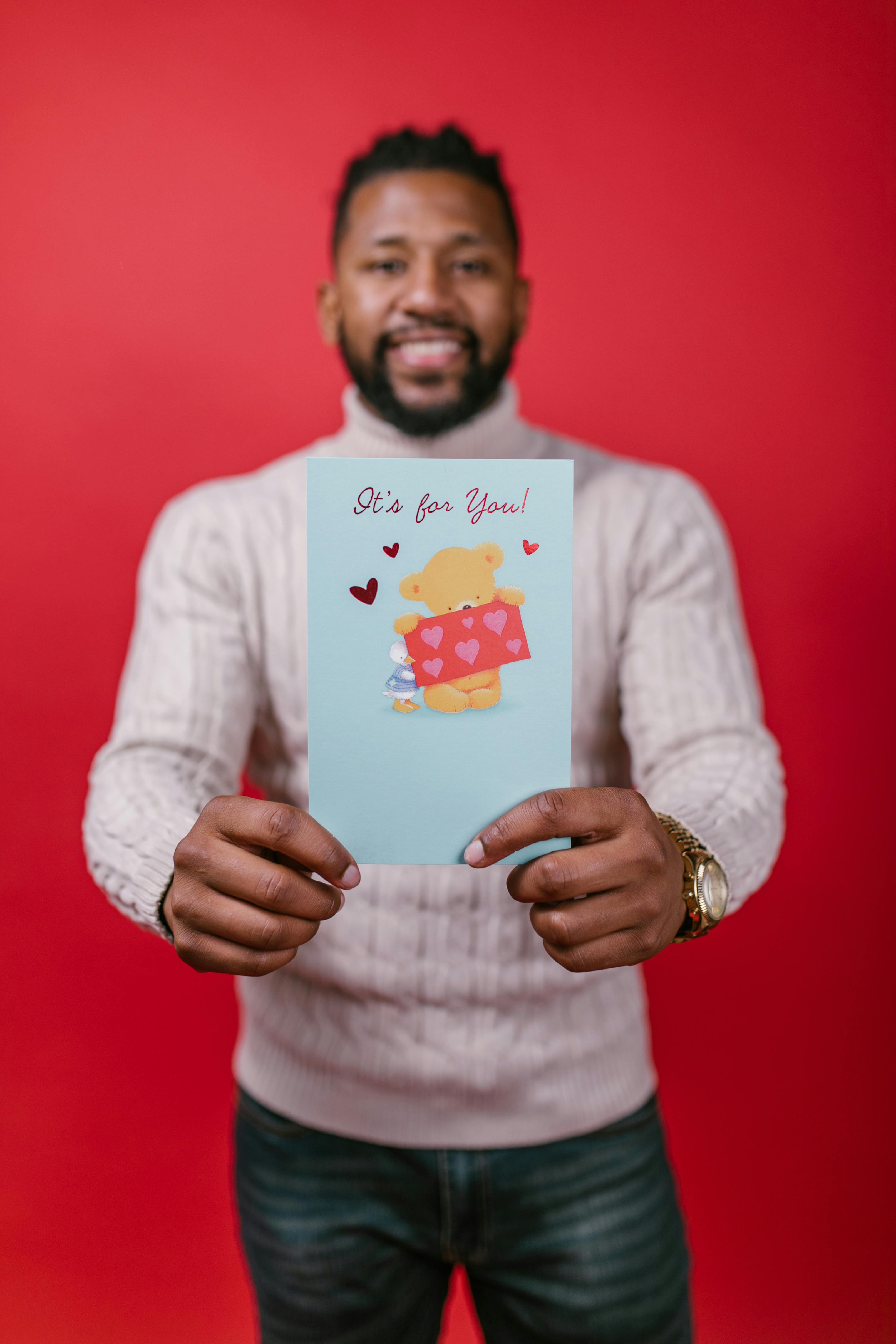 A cheerful man holding a Valentine's Day card with a red background, conveying love and happiness.