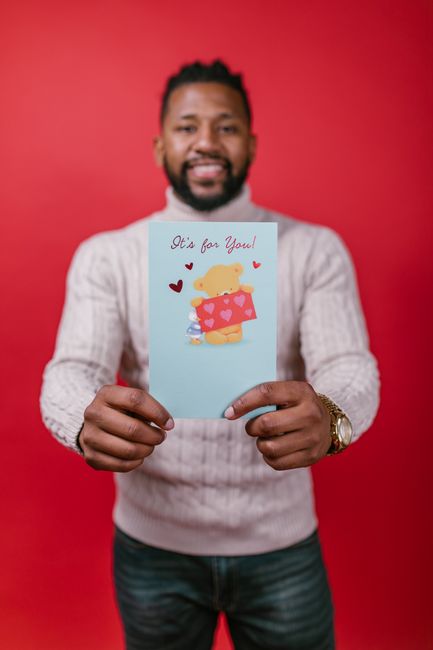 Fotomural Un hombre alegre sosteniendo una tarjeta del Día de San Valentín con un fondo rojo, transmitiendo amor y felicidad.