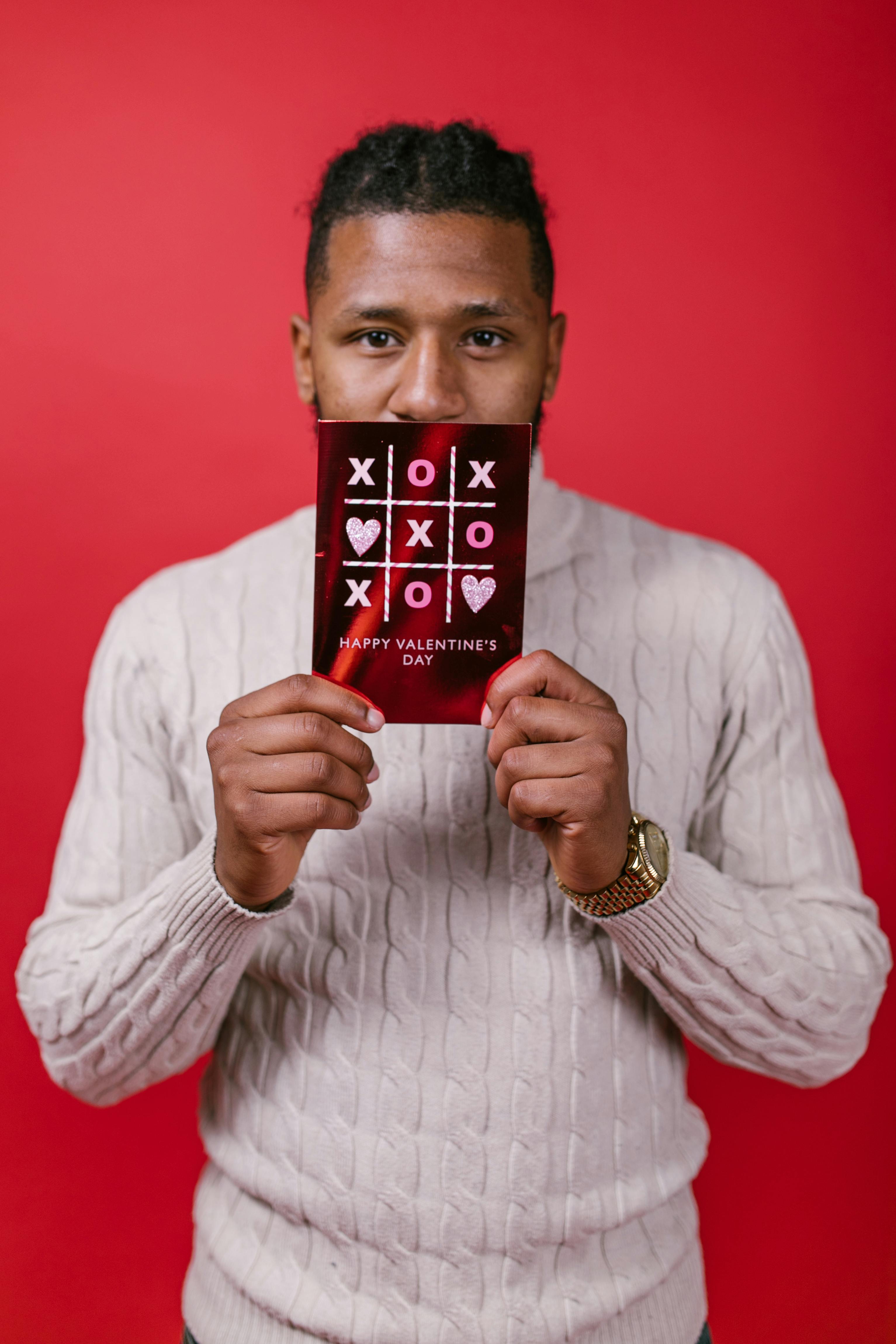 Happy young man holding a Valentine's Day card against a red background.