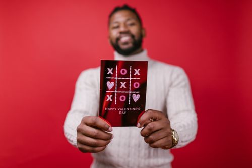 Free A joyful man presenting a Valentine's Day card with a red background, symbolizing love and celebration. Stock Photo