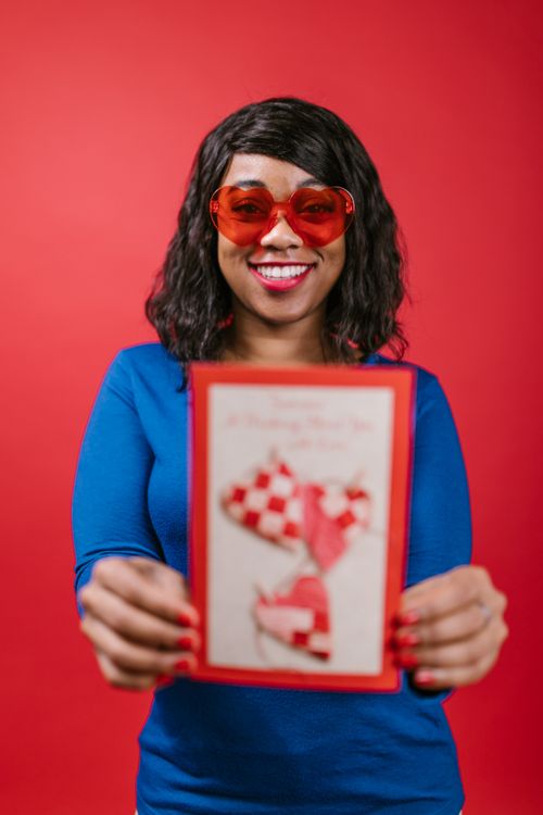 Free Smiling woman in blue holding a Valentine's Day card on a red background. Stock Photo