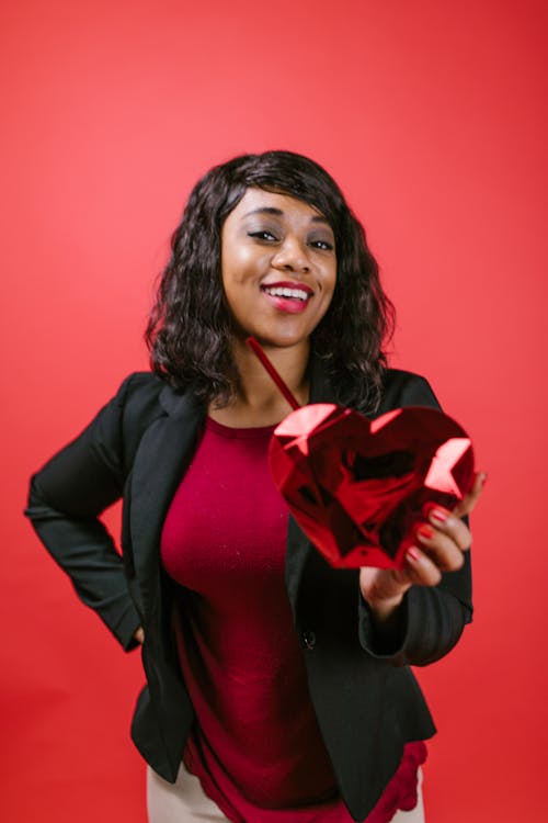 Woman Smiling While Holding a Red Heart Shaped Object